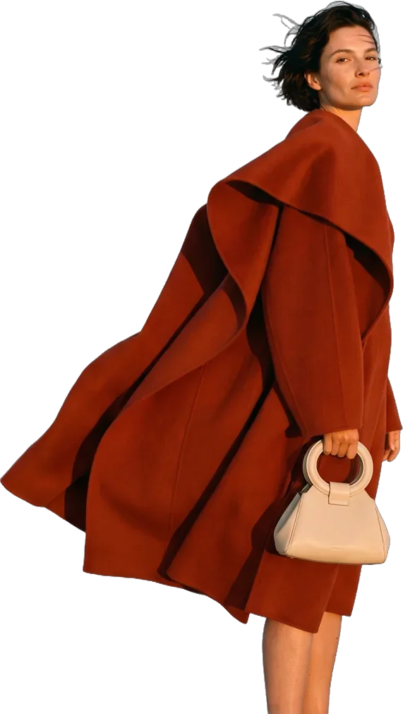 Model in a rust-red coat with a cream handbag, coat blowing in the wind